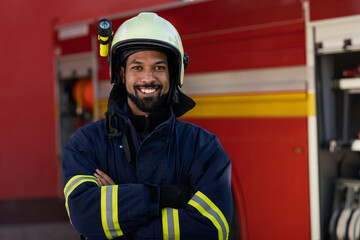 Happy young African-american firefighter man with fire truck in background.