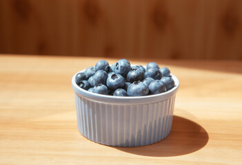 Blueberry berries in blue bowl on the wooden table on the kitchen, summer food