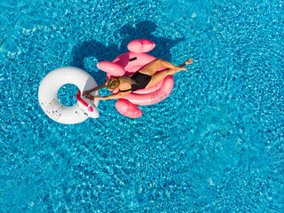 Woman on flamingo pool float and unicorn in pool. Summer holidays, enjoying summer vacations during quarantine.