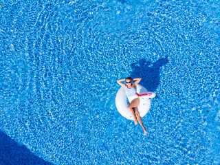 woman relaxing in pool float unicorn inflatable ring floating on turquoise pool water. Aerial top view from drone