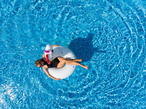 Aerial top view from drone of beach vacation woman relaxing in pool float unicorn inflatable ring floating on turquoise pool water.