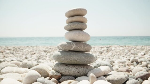 Close-up, a woman makes a cairn. Handmade stone tower on the seashore. A stack of balanced pebbles on the beach. Against the backdrop of the sea