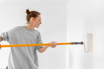 Portrait young adult beautiful single happy woman painting wall paint roller brush white color living room moving new home flat . Female painter decorating interior renovation residential apartment