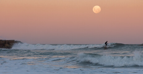 man surfing a wave under the full moon at sunset - Argentina