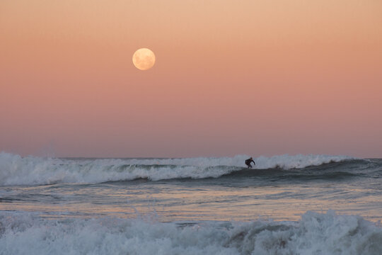 man surfing a wave under the full moon at sunset - Argentina - Powered by Adobe