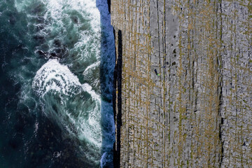 Ocean waves hit cliffs. Rough stone coastline of Aran island, county Galway, Ireland. Aerial top down view. Irish nature landscape.