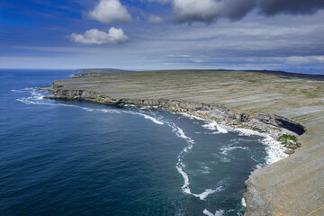 Ocean and cliffs and rugged stone terrain of Aran Island. Warm sunny day and blue cloudy sky. Popular travel tourism destination. Irish landscape.