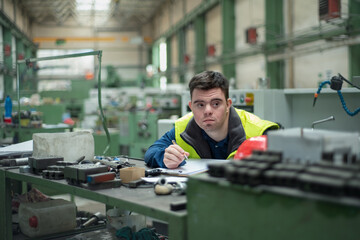 Young man with Down syndrome working in industrial factory, social integration concept.