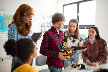 College student presenting his builded robotic toy to young science teacher and his schoolmates at...