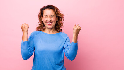 middle age hispanic woman looking extremely happy and surprised, celebrating success, shouting and...