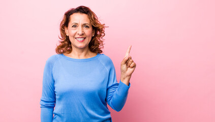 middle age hispanic woman smiling cheerfully and happily, pointing upwards with one hand to copy space - obrazy, fototapety, plakaty