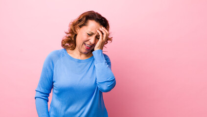 middle age hispanic woman laughing and slapping forehead like saying d’oh! I forgot or that was a...