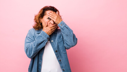 middle age hispanic woman covering face with both hands saying no to the camera! refusing pictures...