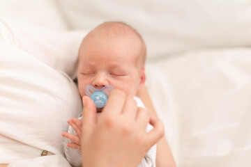 Unrecognizable mother holding her newborn son with dummy at home, close-up