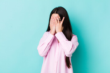 young adult woman feeling scared or embarrassed, peeking or spying with eyes half-covered with hands