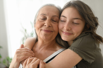 Senior grandmother with teenage granddaguhter hugging together at home.