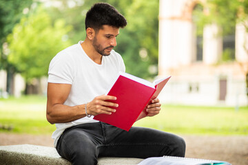 Handsome young man reading book on bench in the park