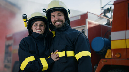 Obraz premium Happy firefighters man and woman after action looking at camera with fire truck in background
