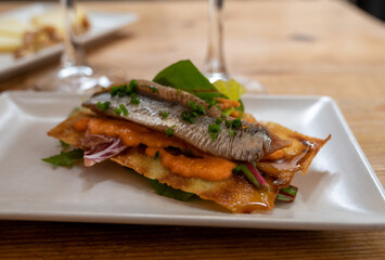 Spanish food, one tapas small piece of roasted bread cracker with vegetables puree and smoked sardine fish