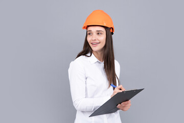 Happy woman in protective helmet with clipboard isolated on grey background. Young woman construction manager. Architect woman, female worker in hardhat helmet.