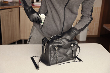 Robber in black outfit and gloves see in opened stolen women bag. The thief takes out the gold and...