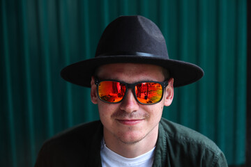 Smiling fashion man. Portrait of handsome smiling stylish hipster lambersexual model. Man dressed in red polarization sunglasses. Fashion male on the modern blue background. Face