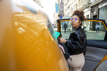 Young African American woman getting into a yellow taxi cab in New York City