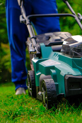 Green lawn mower close-up mows the lawn in the summer garden.Technique and equipment for the garden. Summer work in the garden. A man cuts green juicy grass with a lawn mower in a garden
