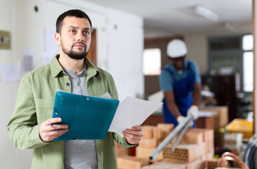 Confident man interior designer planning furnishing and decoration of interior of renovating house, making notes at clipboard