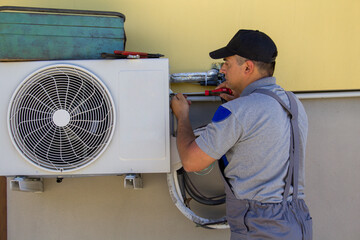 Image of a plumber with tools installing an air conditioner in a house. Reference to the upcoming...