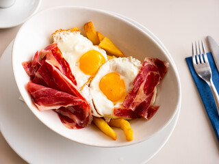 Plate of appetizing hearty breakfast of fried eggs with slices of delicious bacon and French fries