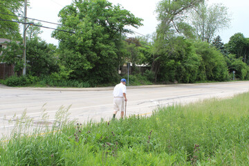 Old man with a cane walking alone on Lehigh Avenue in Morton Grove, Illinois
