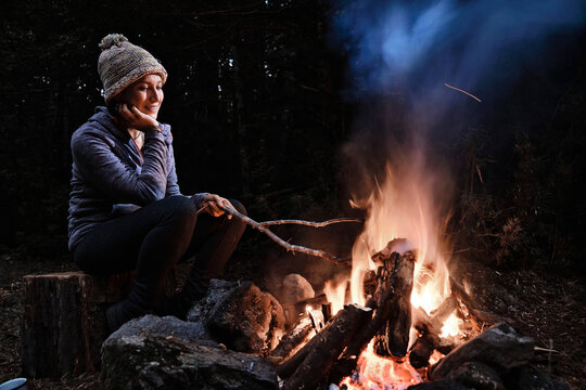 Real woman pensive sitting looking at a campfire and enjoying