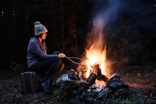 A girl relaxes near a bright campfire with sparks in the middle of the forest