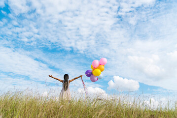 Cheerful cute girl holding balloons running on green meadow white cloud and blue sky with...