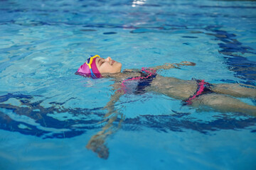 Happy child girl swims in swimming pool. Swim cap and goggles. Training and sports concept.