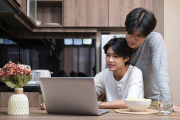 Smiling gay couple using laptop together in home kitchen. LGBT community, equal rights, beauty and love concept.