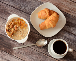 Nice breakfast, bowl of oatmeal with nuts and raisins, two fresh croissants and black coffee.