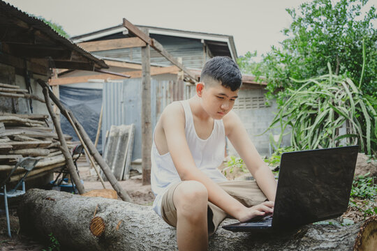 Poor Schoolboy Studying Online With Notebook On Log Behind An Old Country House. Concept Online Education In Countryside Area And Work From Home