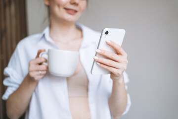 Fototapeta premium Beautiful smiling woman teenager girl student with dark long hair in casual using mobile phone in hand at the home