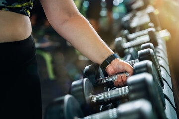 Fototapeta na wymiar Overweight woman hand takes dumbbells in gym closeup. Athletic woman lifting dumbbell weights for exercise in fitness.