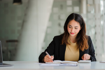 Smiling beautiful Asian businesswoman sitting with laptop and computer working on paperwork make an account analysis report real estate investment information financial and tax system concepts