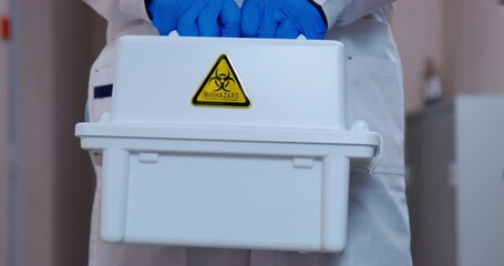 Doctor in sterile protective gloves holds in hands a box for transporting dangerous hazardous bio waste, on which a biohazard warning sticker is pasted, front view, close up