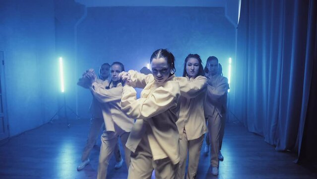 A group of beautiful girls dancing in a room with blue lighting in yellow suits. Dances