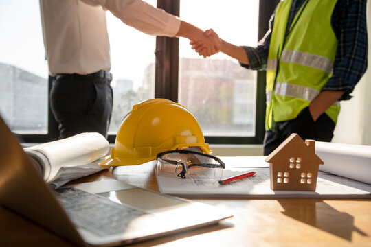 Focused at the desk. behind is Construction workers or architects and engineers shakehands after completing an agreement on an office construction project. Mortgage, rent, buy, sell, move houses.
