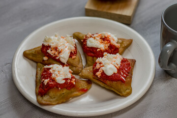 Rich, healthy breakfast of four salty dough empanadas, stuffed with beans, with tomato sauce, cream and cheese.