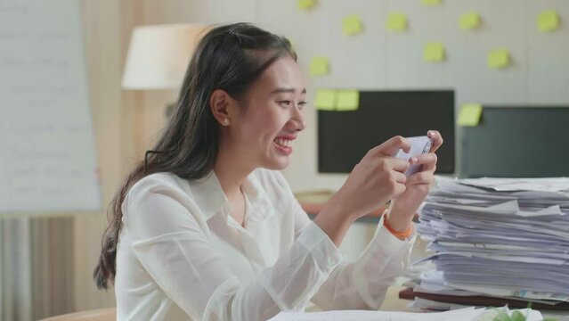 Close Up Of Happy Asian Woman Celebrating Winning Game On Smartphone After Working With Documents At The Office
