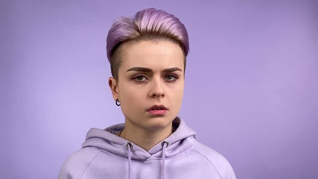 Modern young adult woman turning head left and right gesturing finger on violet color background. Stylish female individuality in trendy hoodie expressing disagreement, denial or rejection. Monochrome