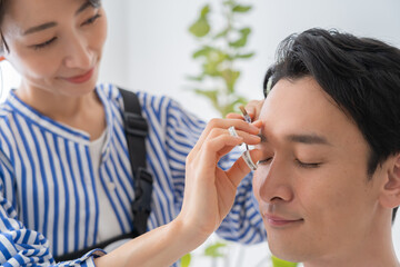 眉毛を整える美容師と日本人男性