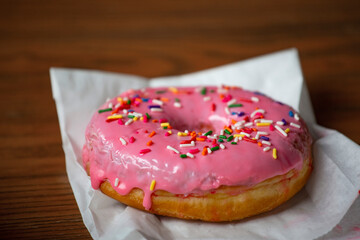 Close up view of a Delicious Pink donut with colorful sprinkles sitting on a table at a coffee shop